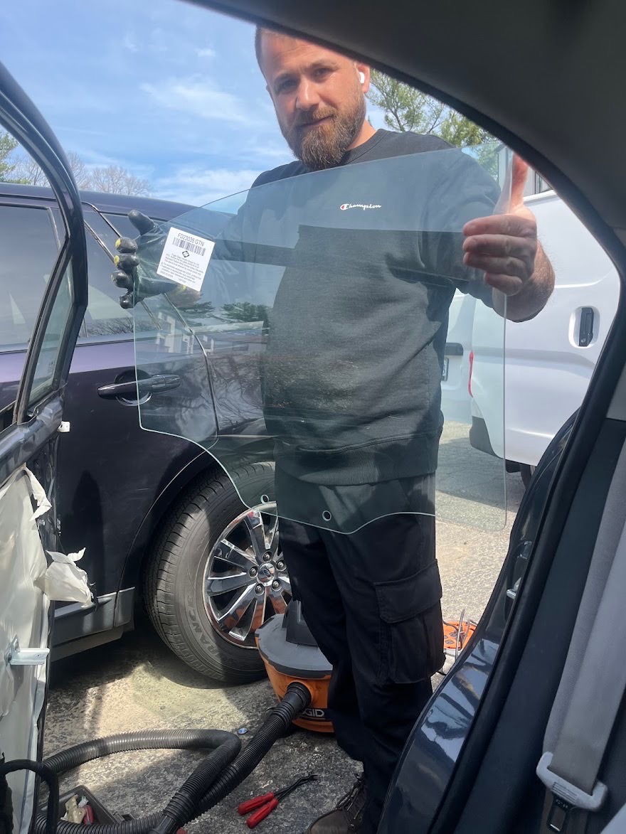 Technician holding a replacement side window glass next to a vehicle