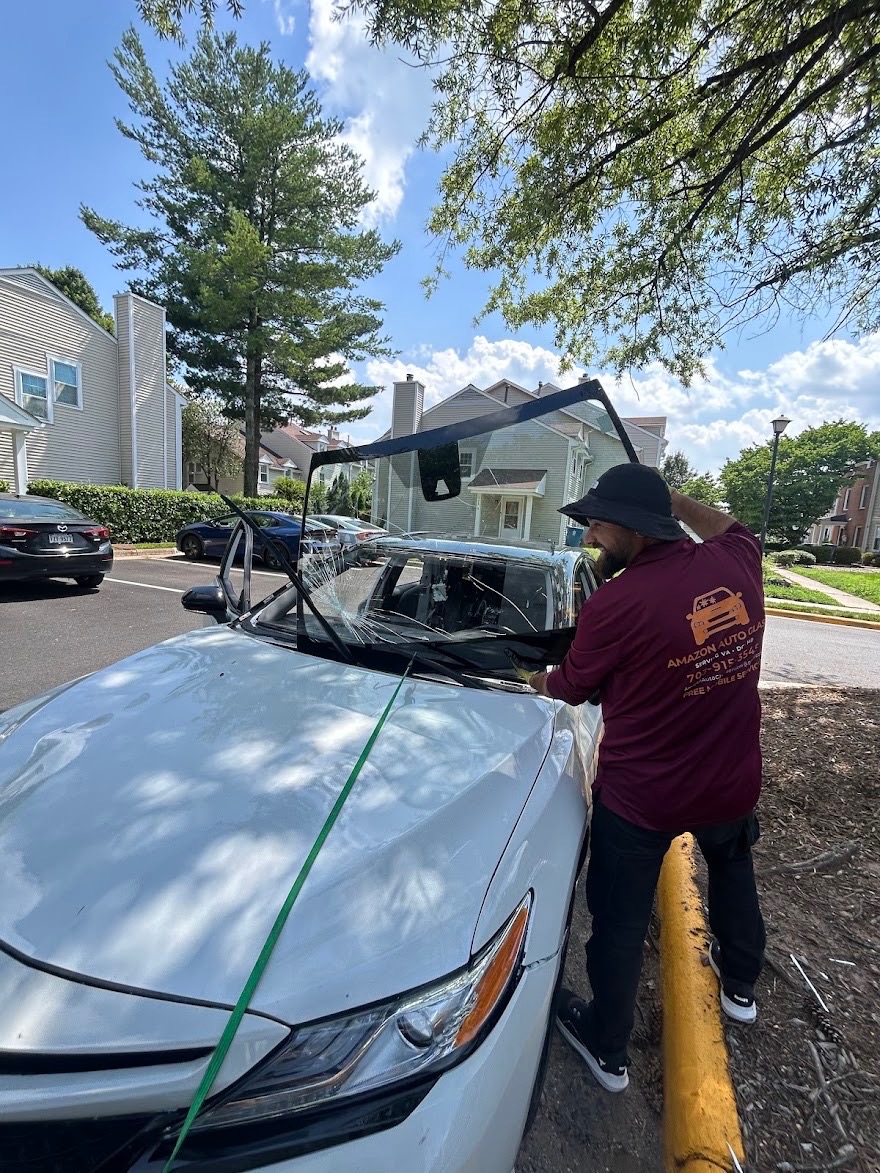 Technician removing rear windshield glass from a white sedan